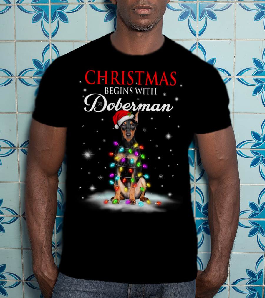 Christmas Begins With Doberman Wrapped In Holiday Lights And Santa Hat Snowflakes T-Shirt